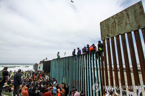 중남미 이민자들이 미국과 맞닿은 멕시코 티후아나의 국경 장벽 앞에 서있다.